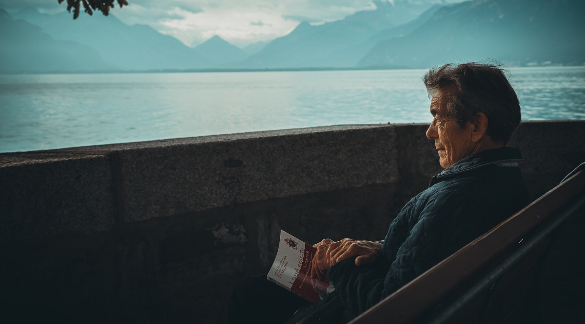 Un home seu davant del mar, mentre llegeix un llibre. Aaron Andrew Ang (Unsplash)