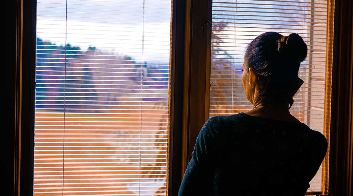 Una dona mira per la finestra de casa seva. Ken Wyatt (Unsplash)