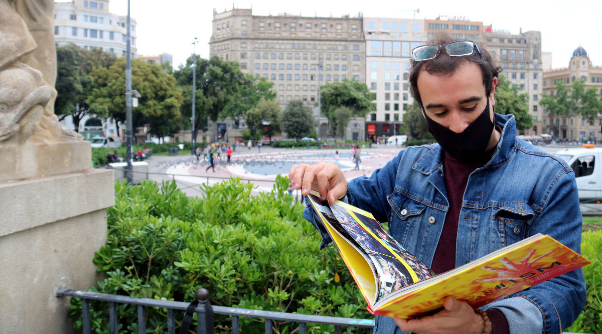 L'activista Ivan Miró mirant un llibre de fotografies del 15-M amb la plaça Catalunya darrere. Pol Solà (ACN)